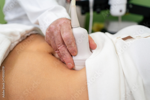 Middle age female patient at abdominal examination checkup with 3D or 4D ultrasound diagnostic scanner. Senior male doctor working at medical clinic. Female healthcare concept.