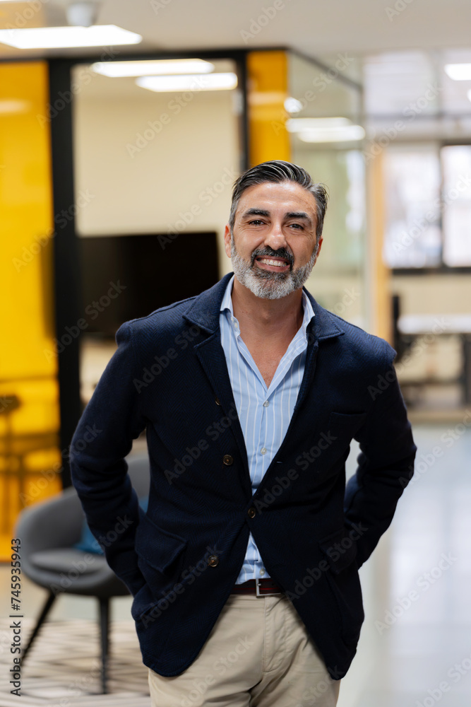 Cheerful mature man with a beard, wearing a blazer, posing in a well-lit office corridor. Cheerful mature man with a beard, wearing a blazer, posing in a well-lit office corridor.