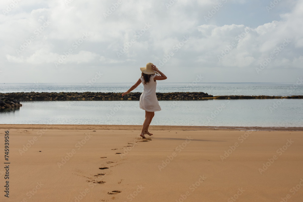 Woman on the beach with hat walking and white dress dancing