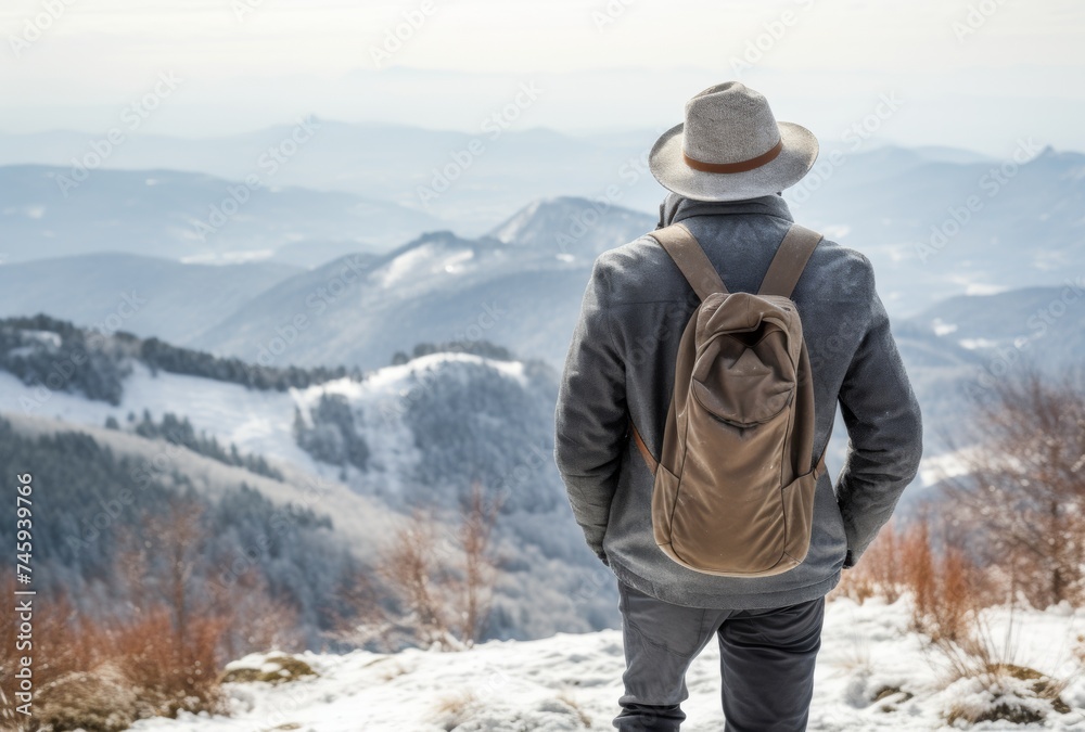 Back view of a hiker with backpack and hat standing on a snow mountain Back view of a hiker with backpack and hat standing on a snow mountain
