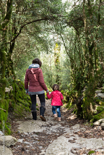 Back view of a mother and her little daughter walking on a forest trail.