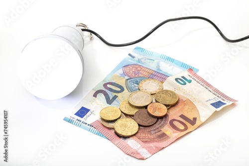 Portable light bulb lit next to money, euro bills and coins on white background. Energy price concept.