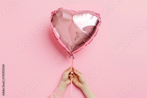 Female hand holding heart shaped balloon. Happy Valentine's Day, birthday, Mother's Day concept. Hand hold pink inflatable foil balloon in a heart shape. Festive concept in front of yellow background.