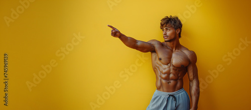 20s handsome tanned muscular man  shirtless  pointing fingers at products or text on yellow background 