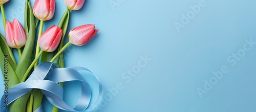 A bouquet of pink tulips is tied together with a blue ribbon, creating a figure in celebration of International Womens Day. The flowers contrast beautifully against the blue background,