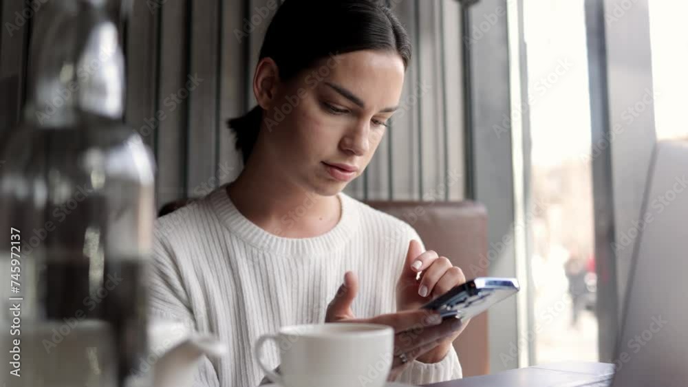 Business woman working online in a modern coffee shop with a smartphone in her hands and a laptop. Concept of freelancing, business, negotiations and remote work. Business woman working online in a modern coffee shop with a smartphone in her hands and a laptop. Concept of freelancing, business, negotiations and remote work.