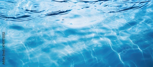 The image shows a pool filled with blue water, creating a serene and refreshing scene. The waters surface is adorned with ripples and rings, which add movement to the tranquil setting.
