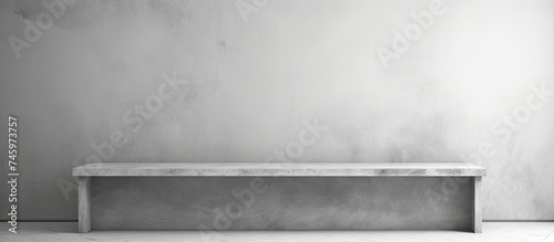 A black and white image showing a bench positioned against a wall in a minimalistic room with a white abstract background. The bench creates a stark contrast against the wall, © Ilgun