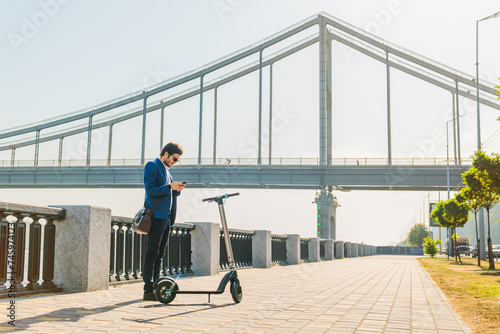 Businessman using cellphone while stopped on electric scooter on city street. Handsome employee male manager using mobile application to unlock the e-transportation © InsideCreativeHouse