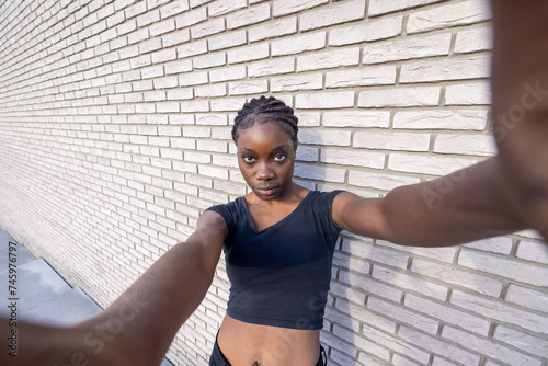 This image captures a young African woman taking a dynamic wide-angle selfie. The perspective is emphasized by her extended arm holding the camera, leading to a slight distortion that adds to the photo