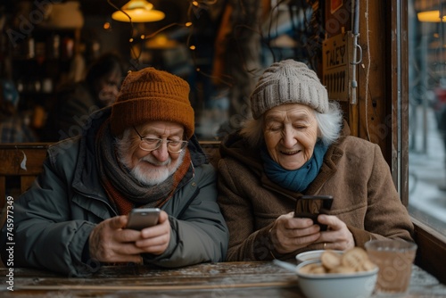 Elderly couple with hats smiles while engaging with their smartphones over coffee