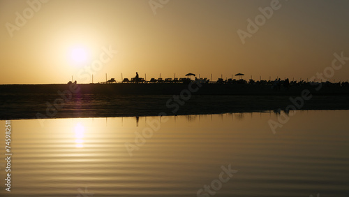 Liegen und Sonnenschirme im Gegenlicht der Abendsonne am Starnd mit Wasser im Vorderund photo