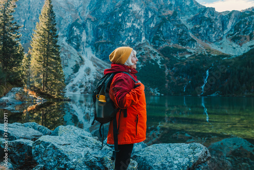 Lady tourist with a backpack standing on top of the mountain and enjoy the beautiful view of mountains Morskie Oko lake. Hiking travel and adventure in Poland, Tatry  photo