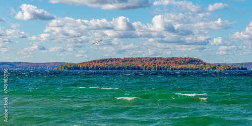 A gull soars over waves and whitecaps with Power Island in Grand Traverse Bay, Michigan in the background