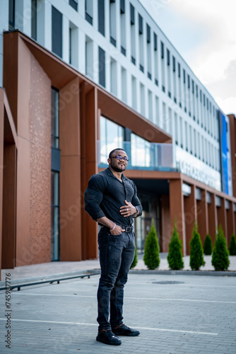 Bald brutal man in black T-shirt and jeans stands on the background of modern building, bald brutal man in black T-shirt and jeans stands on the background of modern building © Vadim