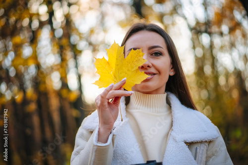 Beautiful young woman walks in the autumn park and holds yellow maple leaves in her hands  Beautiful young woman walks in the autumn park and holds yellow maple leaves in her hands