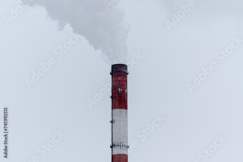 Pipe of a thermal power plant expels a dramatic plume of steam into the overcast sky, highlighting the intersection of industry and the environment.