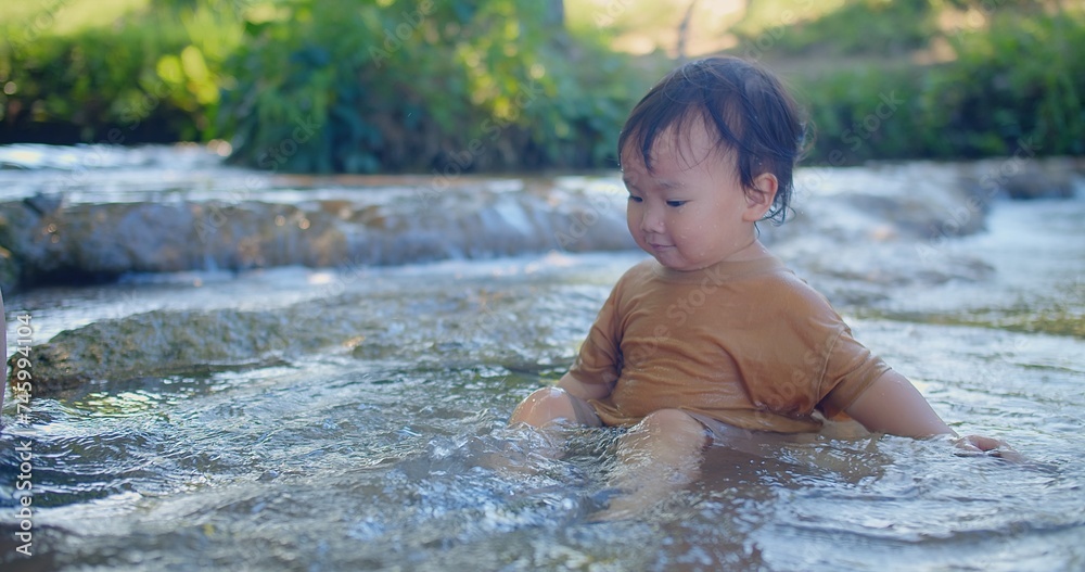 Exuberant toddler splashing in a shallow stream, laughter sparkling as sunlight filters through green foliage in a blissful outdoor scene Exuberant toddler splashing in a shallow stream, laughter sparkling as sunlight filters through green foliage in a blissful outdoor scene