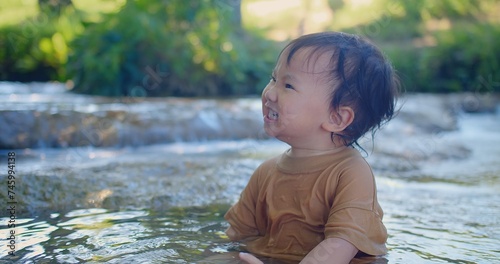 Fototapeta Naklejka Na Ścianę i Meble -  Exuberant toddler splashing in a shallow stream, laughter sparkling as sunlight filters through green foliage in a blissful outdoor scene