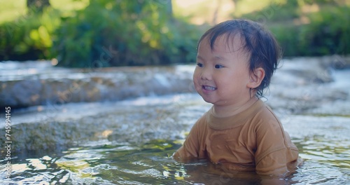 Fototapeta Naklejka Na Ścianę i Meble -  Exuberant toddler splashing in a shallow stream, laughter sparkling as sunlight filters through green foliage in a blissful outdoor scene
