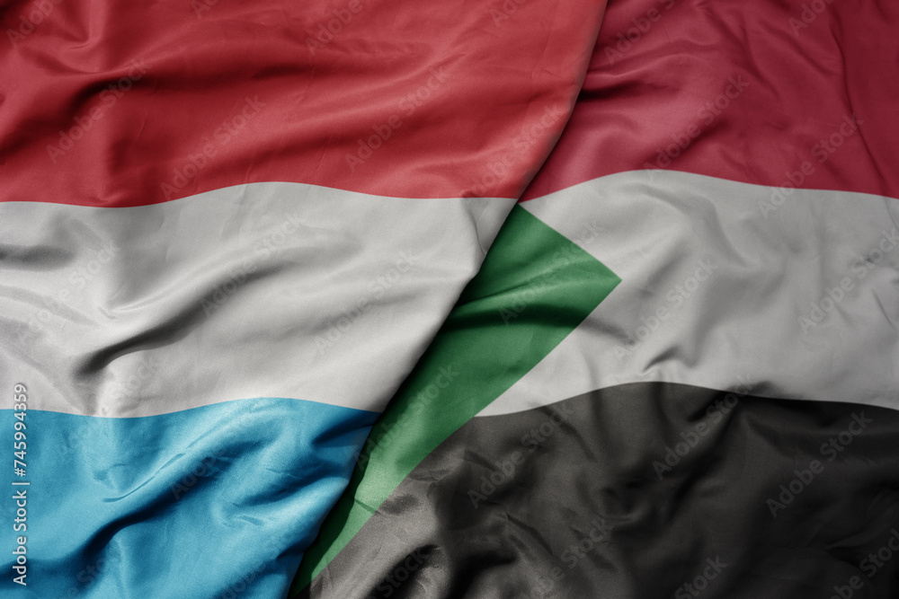 big waving national colorful flag of sudan and national flag of luxembourg .