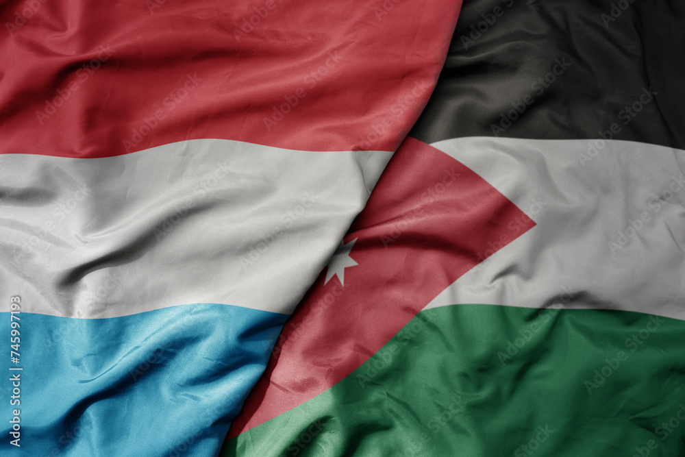 big waving national colorful flag of jordan and national flag of luxembourg .