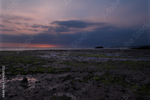 Anochecer con sol detras de las nubes y luces rojizas i violetas con algas verdes en Ujung Genteng, Sukabumi, Java, Indonesia photo