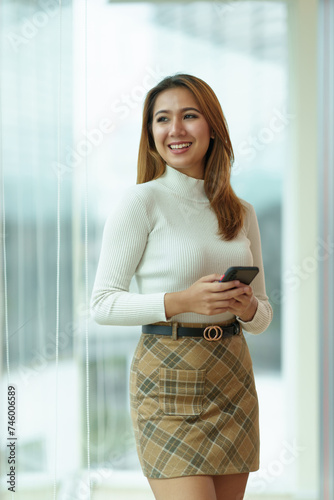 Free Download Smiling asian businesswoman using smartphone in modern office building. Professional lifestyle and communication technology concept - GFXLoad