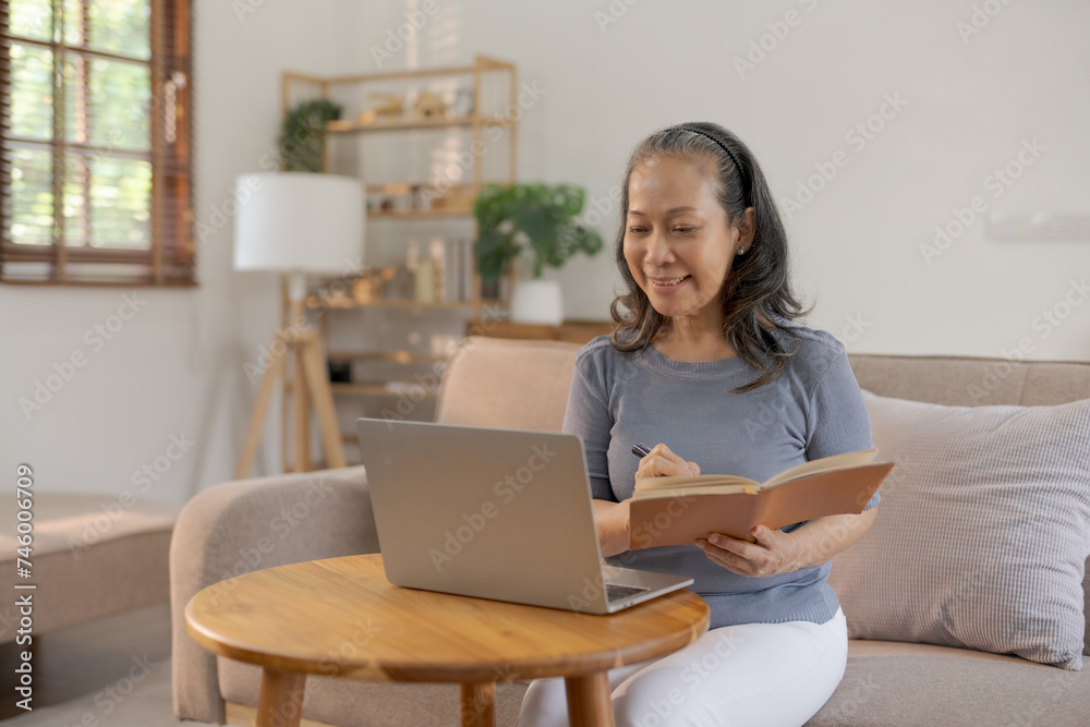 Mature asian woman studying with notebook and laptop at home. Casual indoor learning and education concept. Mature asian woman studying with notebook and laptop at home. Casual indoor learning and education concept.