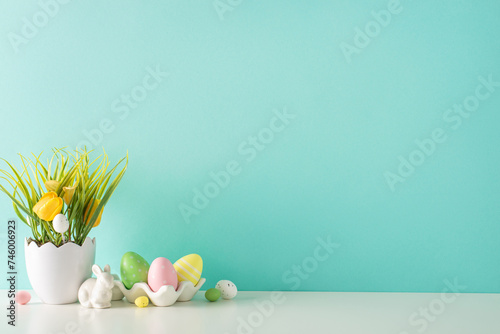 Easter decor idea: A side view of a tabletop displaying a shell-inspired planter with tulips and grass, a ceramic hare, and multicolored eggs in holder, all against a pastel turquoise wall photo