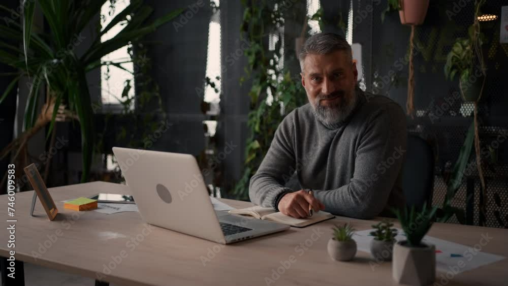 Smiling mature guy takes notes watching webinars on the laptop, researching business tasks Smiling mature guy takes notes watching webinars on the laptop, researching business tasks