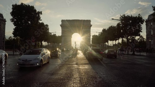 This is the triumphal arch, an important historical monument. In the backlight we see people crossing the street and cars driving with a beautiful sunset behind the arch. photo