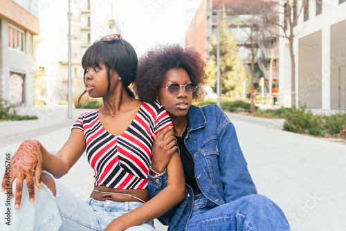 Two sisters share a moment on a city sidewalk, their casual styles and relaxed postures capturing the essence of urban life photo