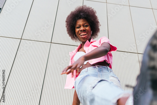 From below of joyful young woman laughing candidly, her vibrant pink shirt and casual denim creating a perfect blend of urban chic and carefree spirit photo