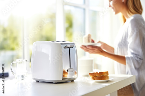 White toaster on a kitchen counter table. A woman in a sunlit minimalist interior kitchen cooking fresh toast breakfast from bread. Concept of tranquil morning routine with cozy light and comfort