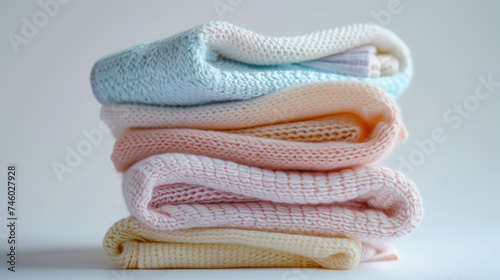 Stacked baby knitwear in pastel shades on a white background.