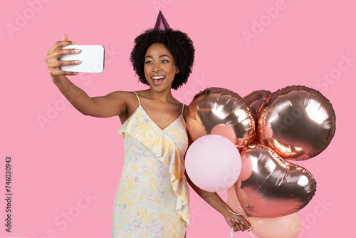 Excited African American woman with curly hair taking a selfie, wearing a party hat