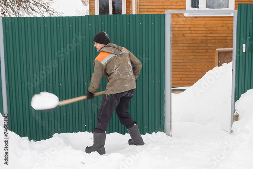 Photo in motion. A European man removes snow in front of the gate of his house.