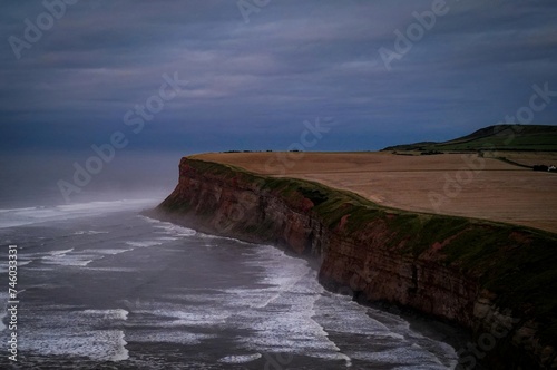 an empty beach with a cliff next to the ocean with waves in it