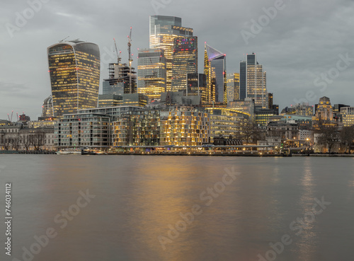 The illuminated of skyscraper in the business district of London with reflections in the River Thames just after sunset. View of architectural modern buildings of the city, Copy space, Selective Focus