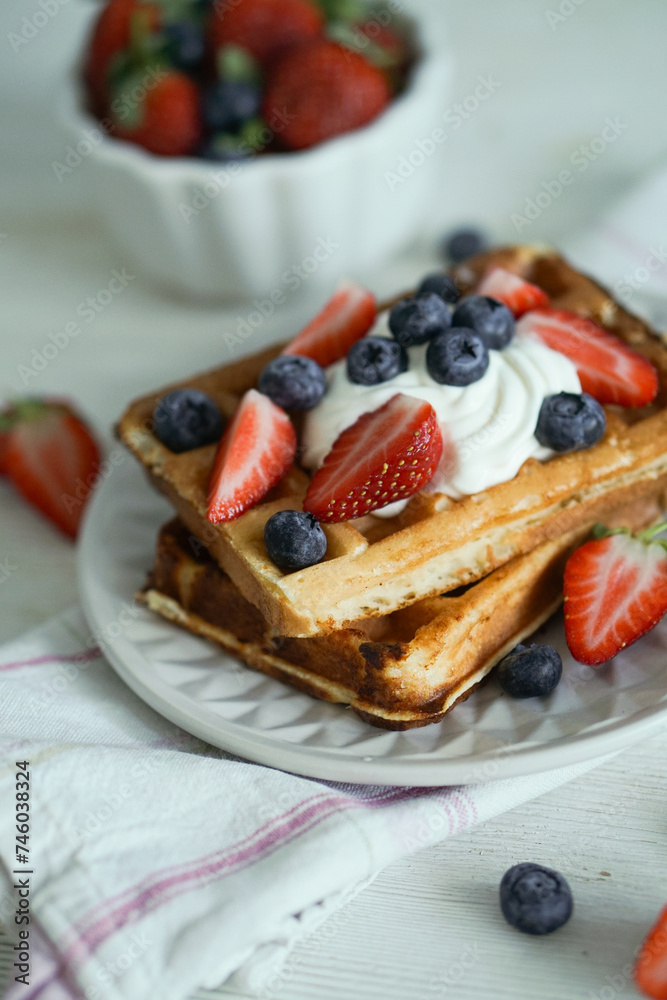 Home made waffles with whipped cream on top and fresh strawberries and blueberries perfect for breakfast close up selective focus