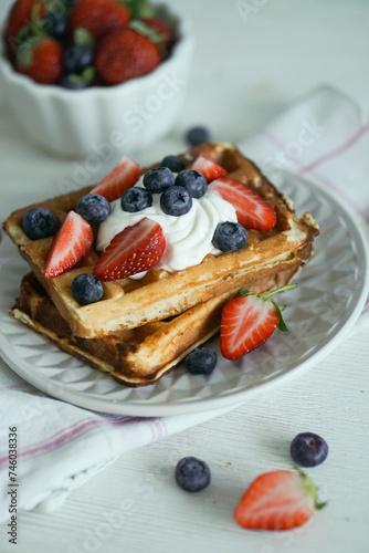 Home made waffles with whipped cream on top and fresh strawberries and blueberries perfect for breakfast close up selective focus