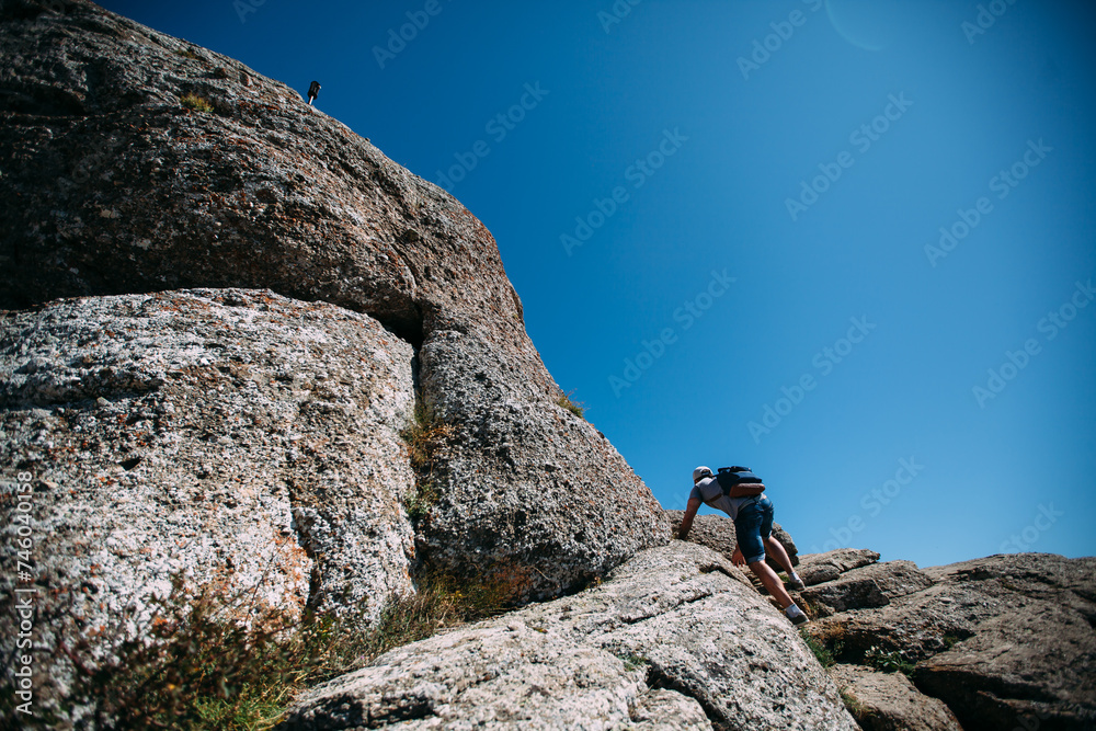 A male tourist with a backpack climbs the mountains to the top. Mountain tourism. Hiking in the mountains in summer