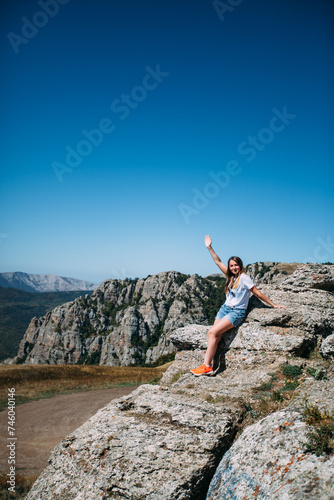 A female tourist on the background of a mountain landscape raised one hand up in greeting. Mountain tourism. Hiking in the mountains in summer