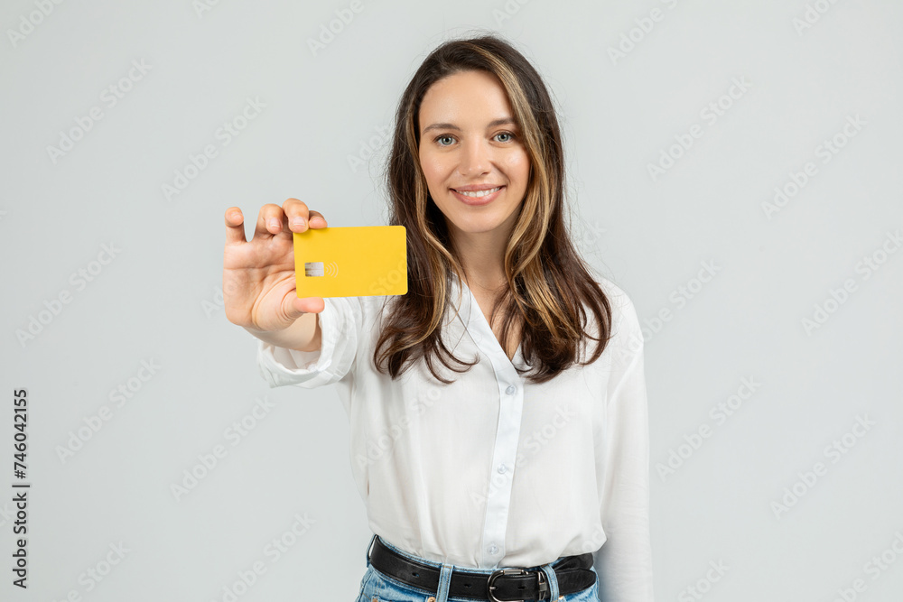 Approachable young woman presenting a yellow credit card with a chip and contactless symbol Approachable young woman presenting a yellow credit card with a chip and contactless symbol