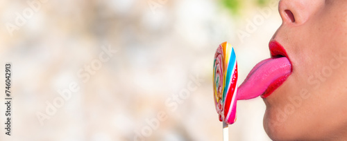 Long  pink and sensual tongue touching and tasting a colorful spiral lollipop with its tip. Sensual bright red lips. Latin woman with dark skin.