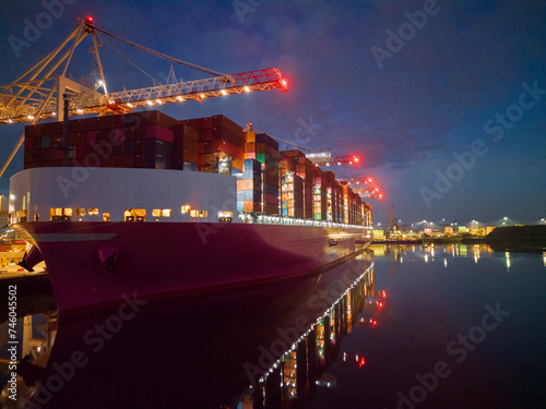 Obraz na płótnie Pink container ship at night at Southampton Docks, UK. Aerial view of the bow and side view of the vessel loaded with shipping containers. Calm sea with ship and port crane lights reflection. w salonie