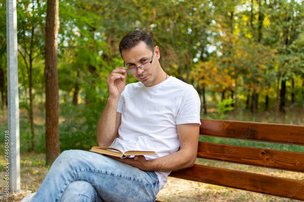 A guy in glasses sits on a bench in the park and reads a book A guy in glasses sits on a bench in the park and reads a book