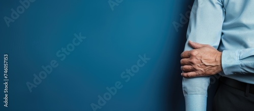 Diverse stock photo of a man with wrist pain in office attire on blue wall background photo