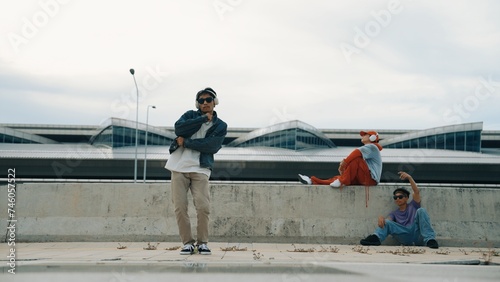 Handsome break dancer enjoy perform freestyle movement with asian friend cheering behind. Hipster listen to music from headphone and looking at camera. Street dance. Outdoor sport 2024. Sprightly.